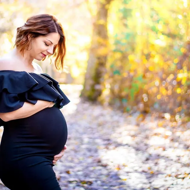 cover galerie Femme enceinte se tenant le ventre, dans un sentier recouvert de feuilles mortes automnales, lumière filtrée.