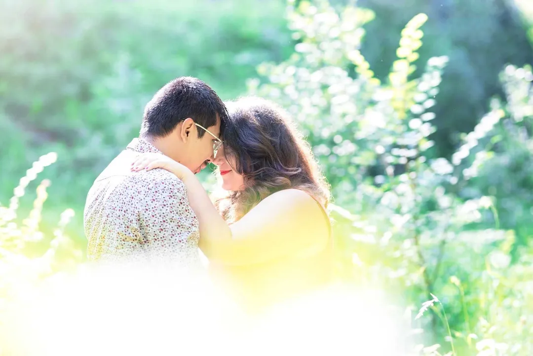 Couple au premier plan, dans un champ de fleurs blanches, un homme portant un chemisier à motifs roses et blancs, une femme vêtue d'une robe jaune clair, regardant l'un l'autre avec affection.