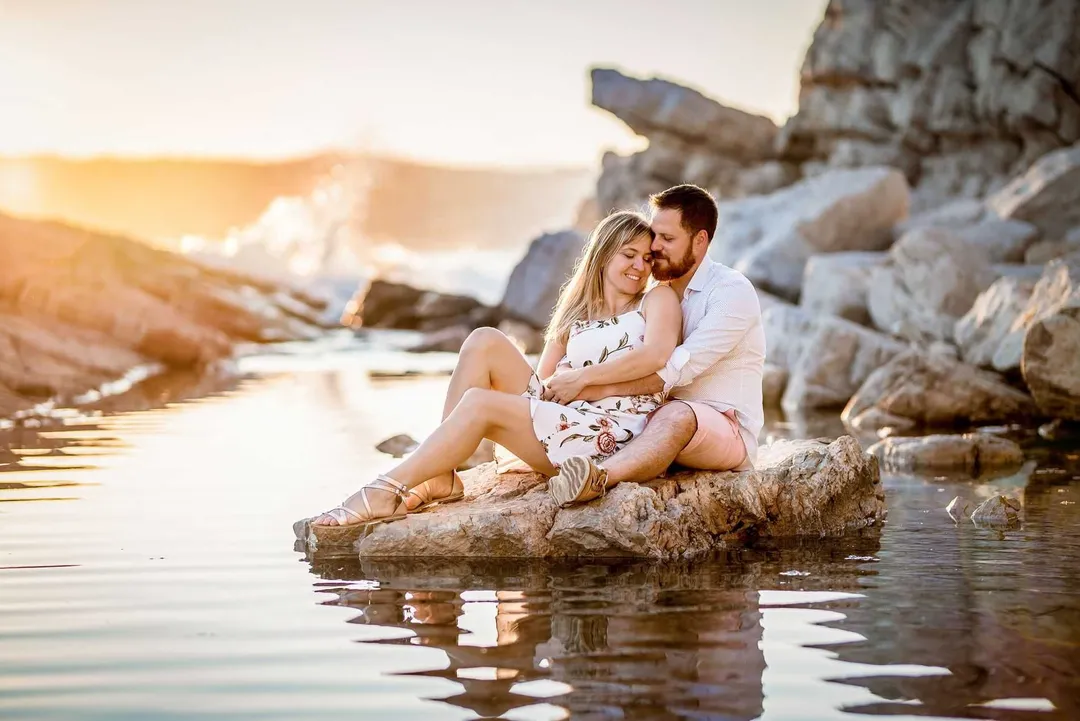 Couple heureux s'embrassant sur un rocher au bord de l'eau lors d'un shooting photo de mariage.