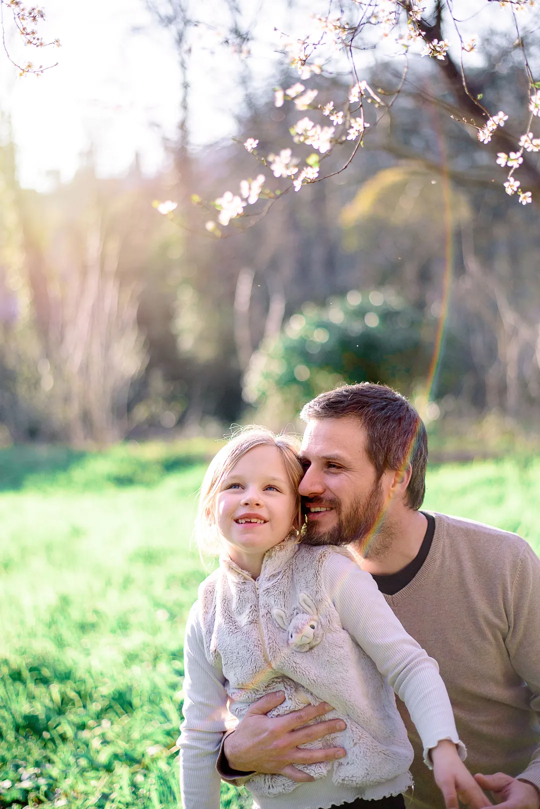Un père et sa fille riant ensemble dans un champ verdoyant au printemps.