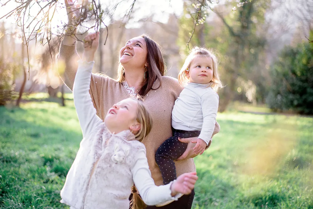 Une maman et sa fille sourient et tendent les bras vers le ciel dans un jardin verdoyant au printemps.
