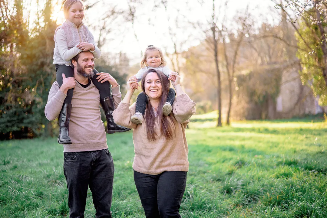 Un père portant sur son dos sa fille dans un parc verdoyant au printemps.