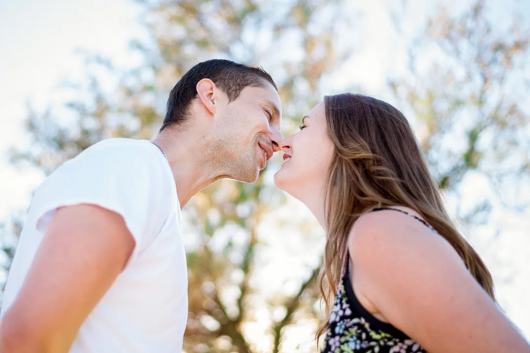 Couple s'embrassant dans un environnement ensoleillé et arboré.