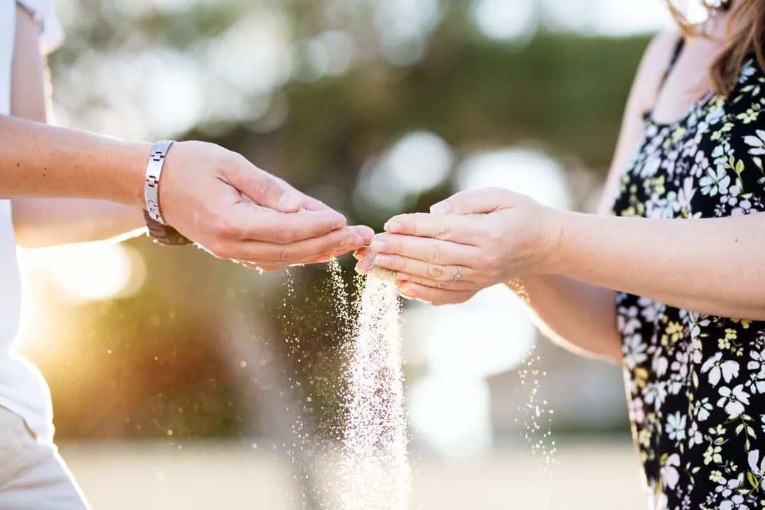 Deux mains se tendent, se touchant avec de la poudre, symbolisant l'épanouissement et le partage d'un nouveau commencement.