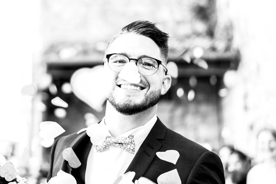 Marié souriant au milieu de pétales de roses, dans un cadre boisé et romantique.