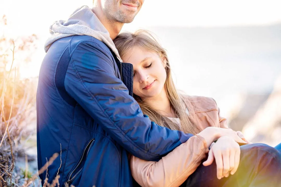 Un couple s'embrasse sur le bord de mer, vêtu de vêtements chauds et enveloppé dans une atmosphère douce.