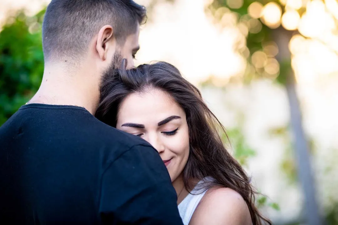 Couple enlacé dans un environnement boisé ensoleillé.