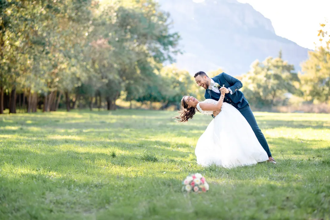 Mariée en robe blanche, tourbillon joyeux avec son mari dans un champ verdoyant.