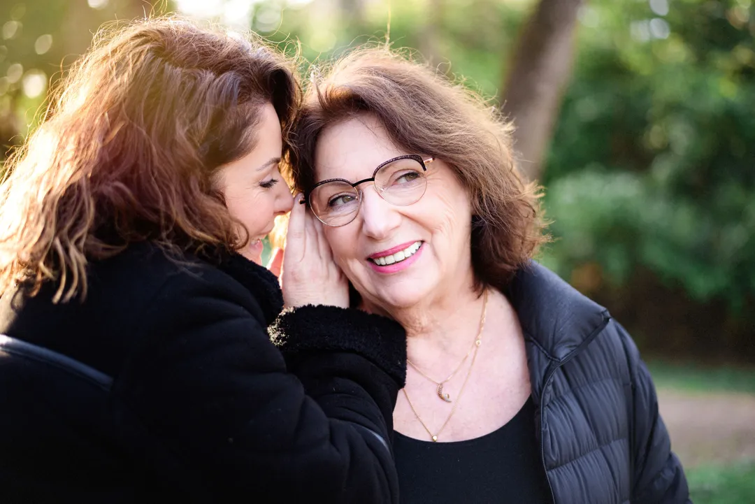 Une grand-mère et sa petite-fille s'embrassent et partagent un secret dans un parc ensoleillé.