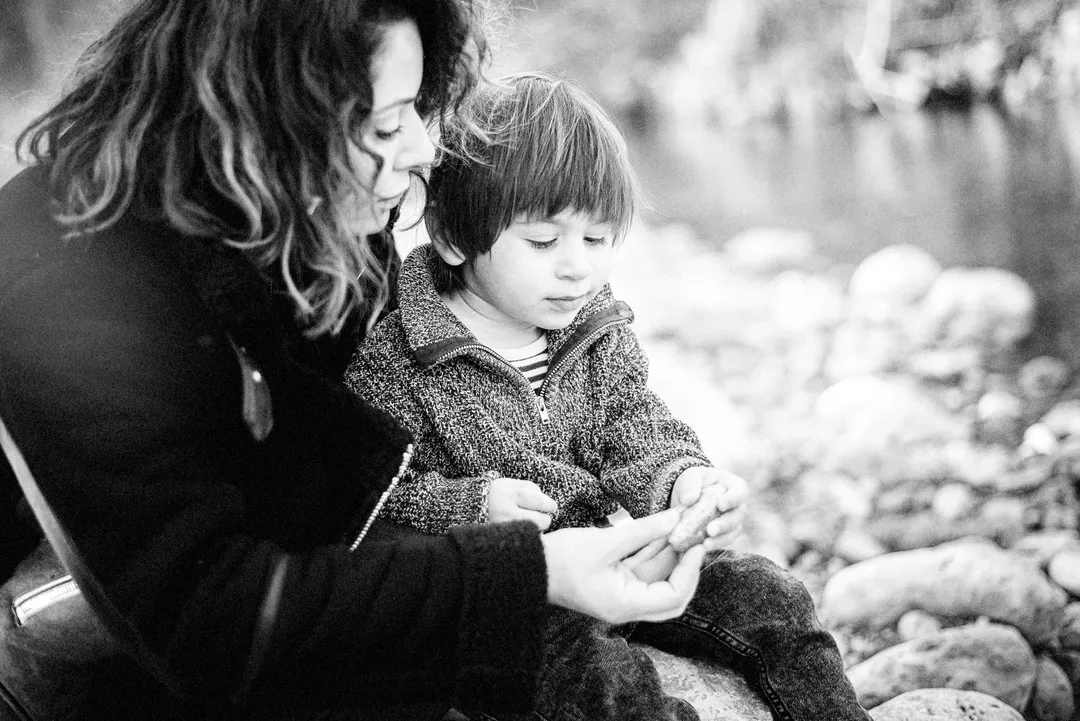 Un jeune garçon est assis sur des pierres, concentré sur un petit morceau de bois qu'il tient dans ses mains.