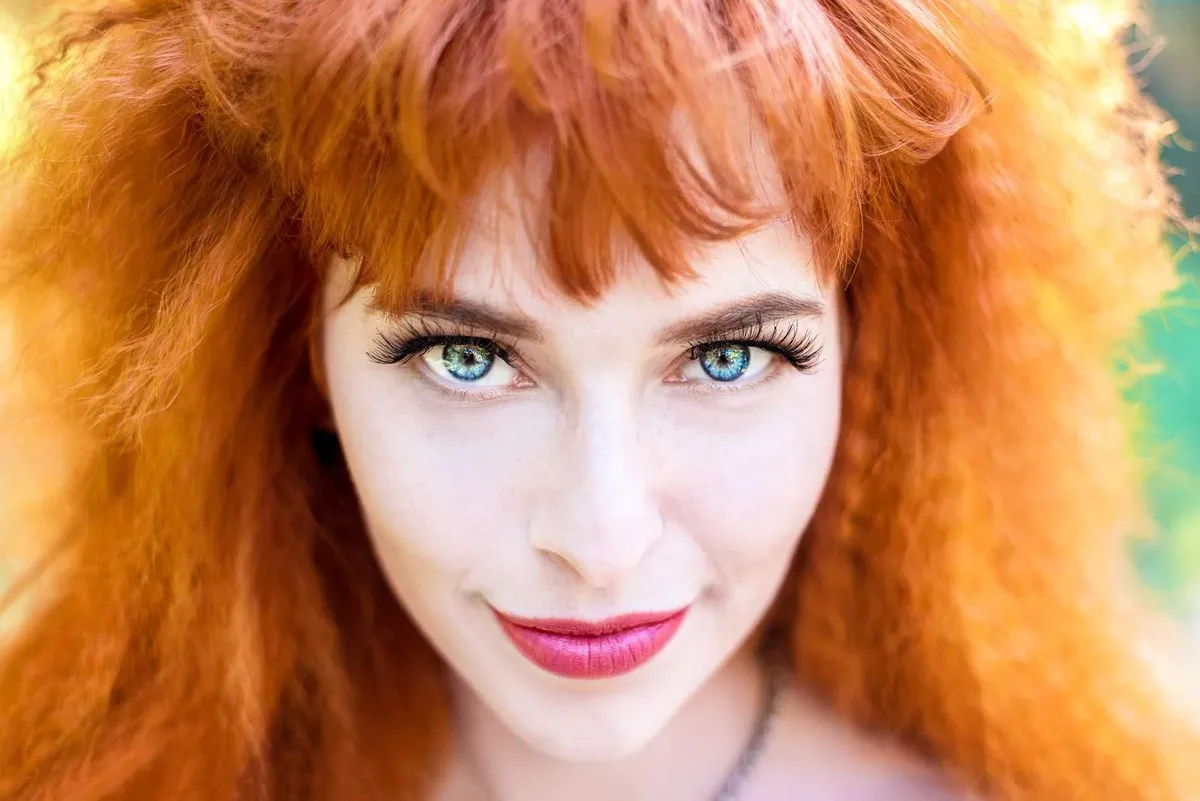 Femme rousse aux longs cheveux ondulés, sourire éclatant.