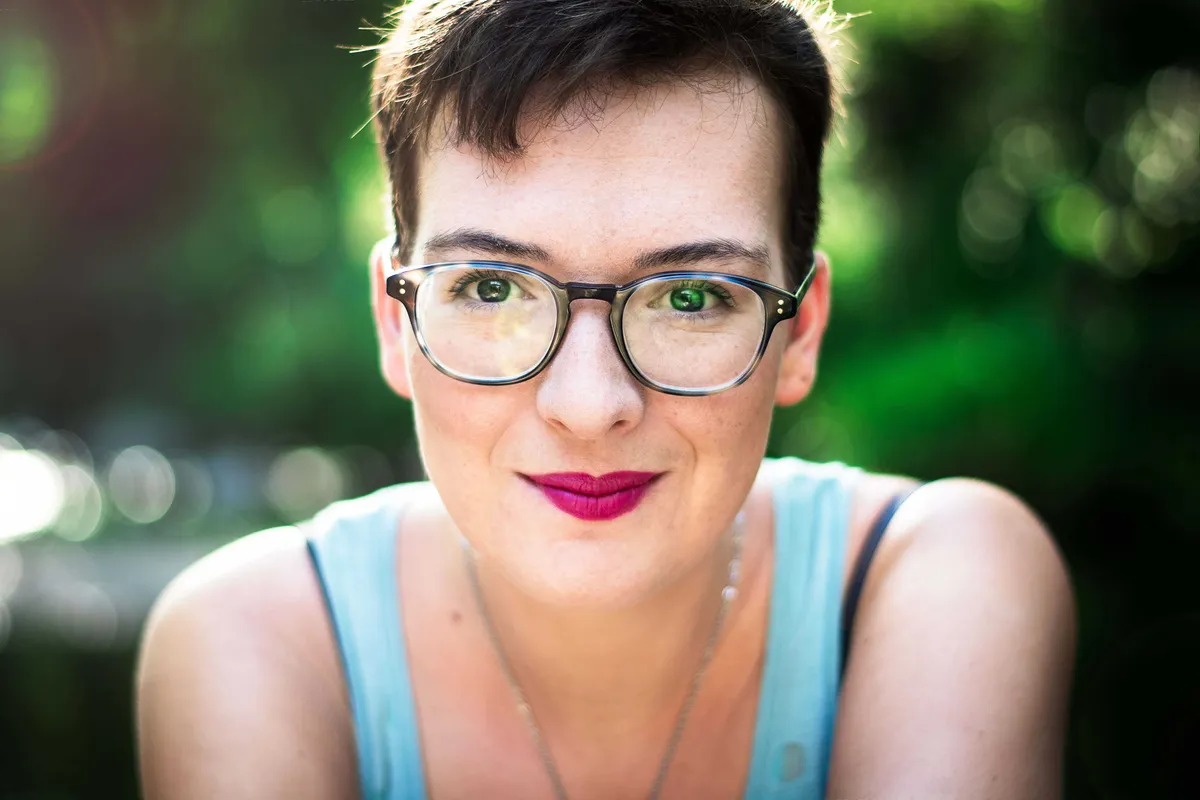 Portrait d'une jeune femme souriante portant des lunettes et un maquillage léger, se concentrant sur la caméra.