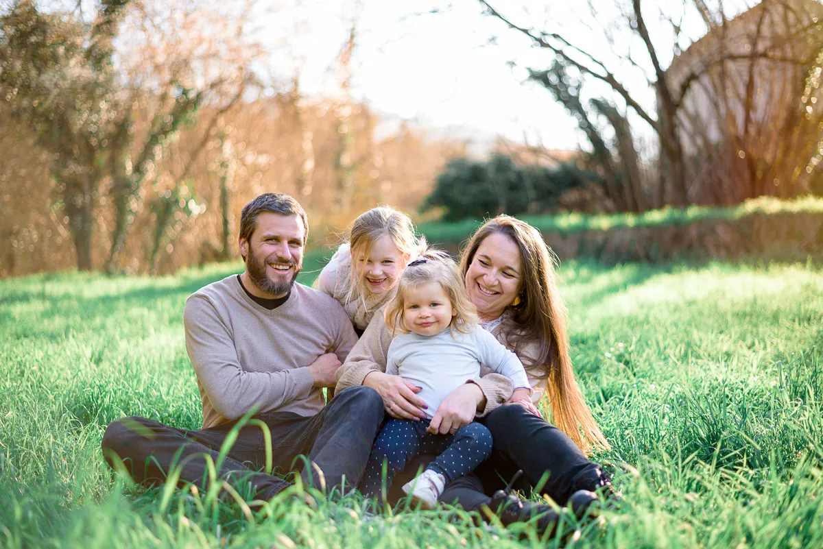 Un père, sa fille et sa femme se blottissent ensemble dans un champ vert, souriants et heureux.