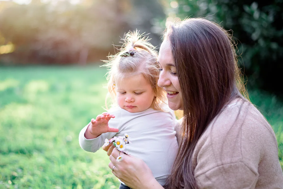 Une jeune fille tient délicatement une marguerite dans ses mains, son visage expressif et souriant.