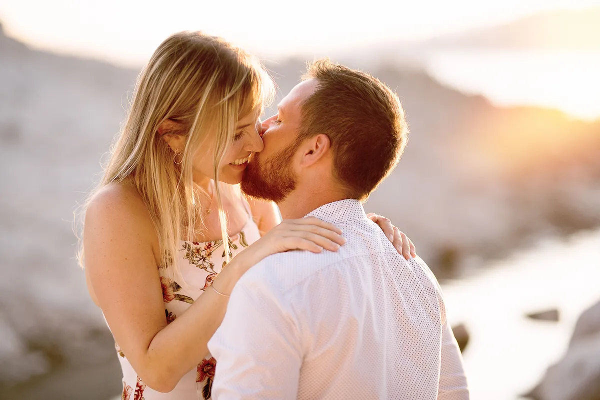 Couple étreint au coucher du soleil sur un paysage rocheux et marin.