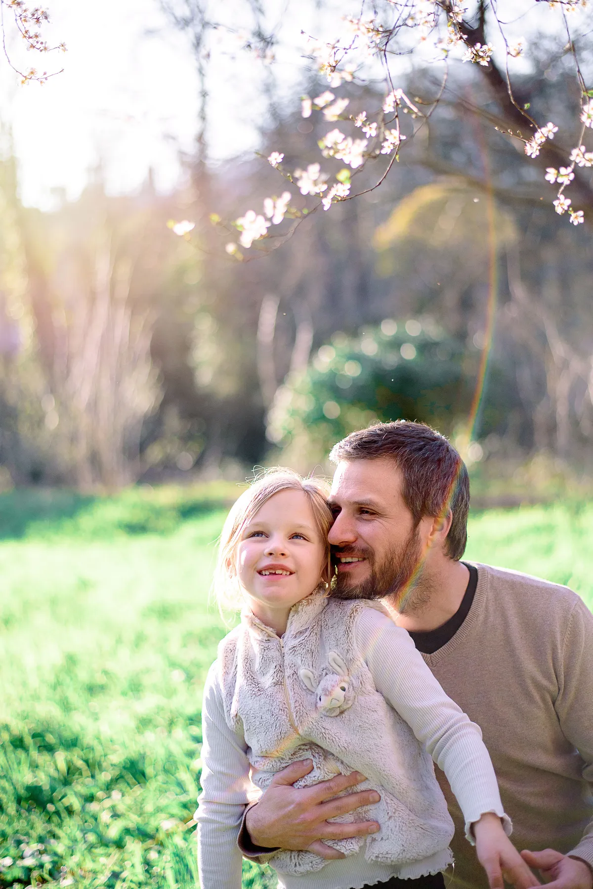 Un père et sa fille riant ensemble dans un champ verdoyant au printemps.