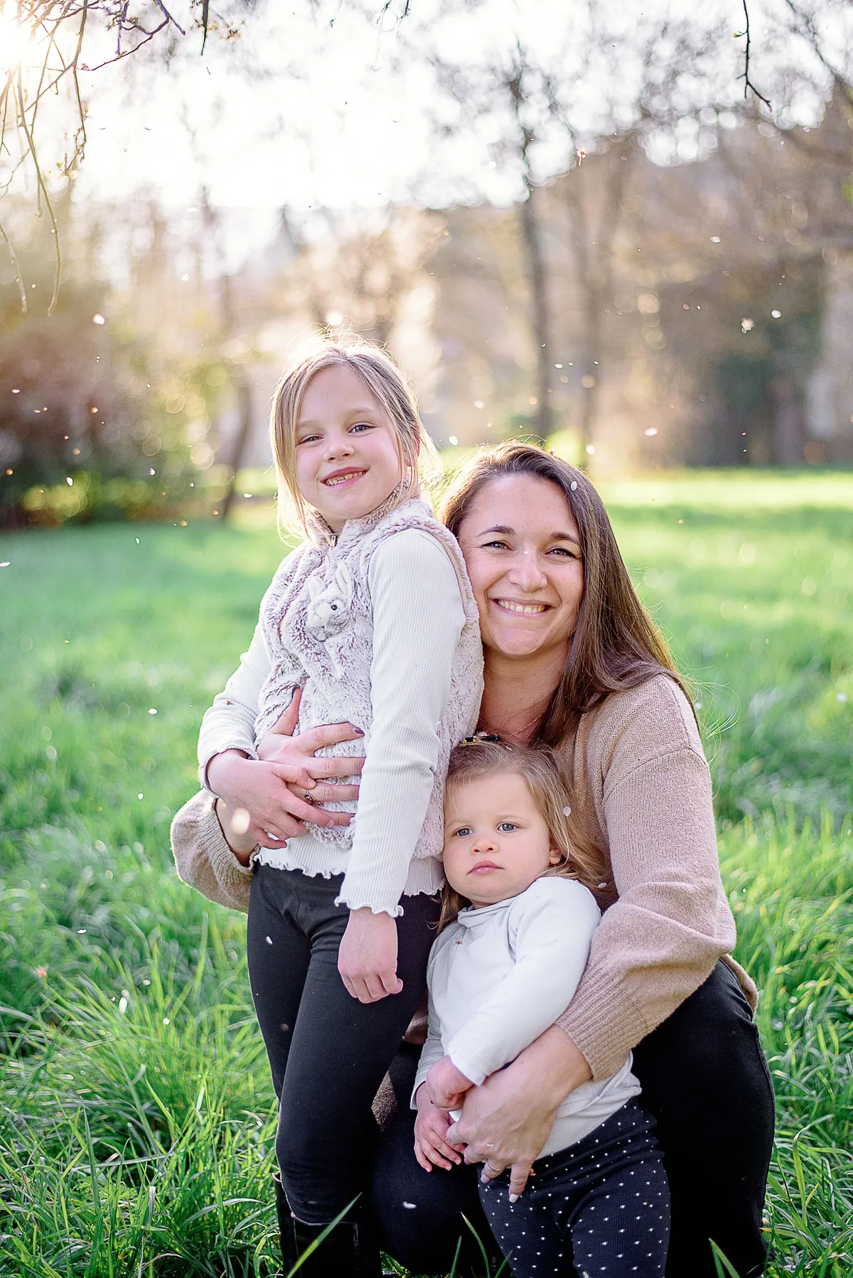 Maman et ses filles souriantes dans un champ verdoyant jonché de fleurs printanières.
