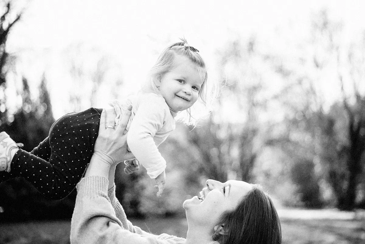 Une petite fille souriante est soulevée dans les bras de sa maman.