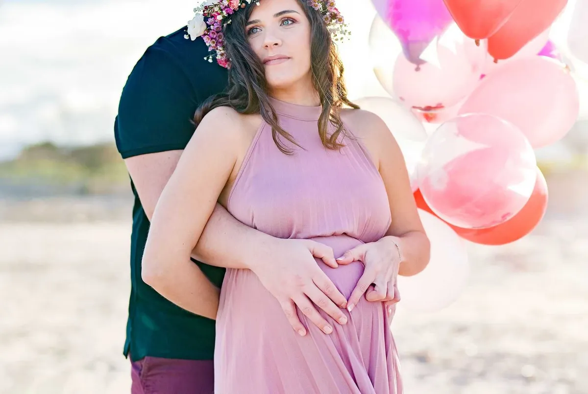 Femme enceinte tenant son ventre en forme de cœur, entourée de ballons colorés.