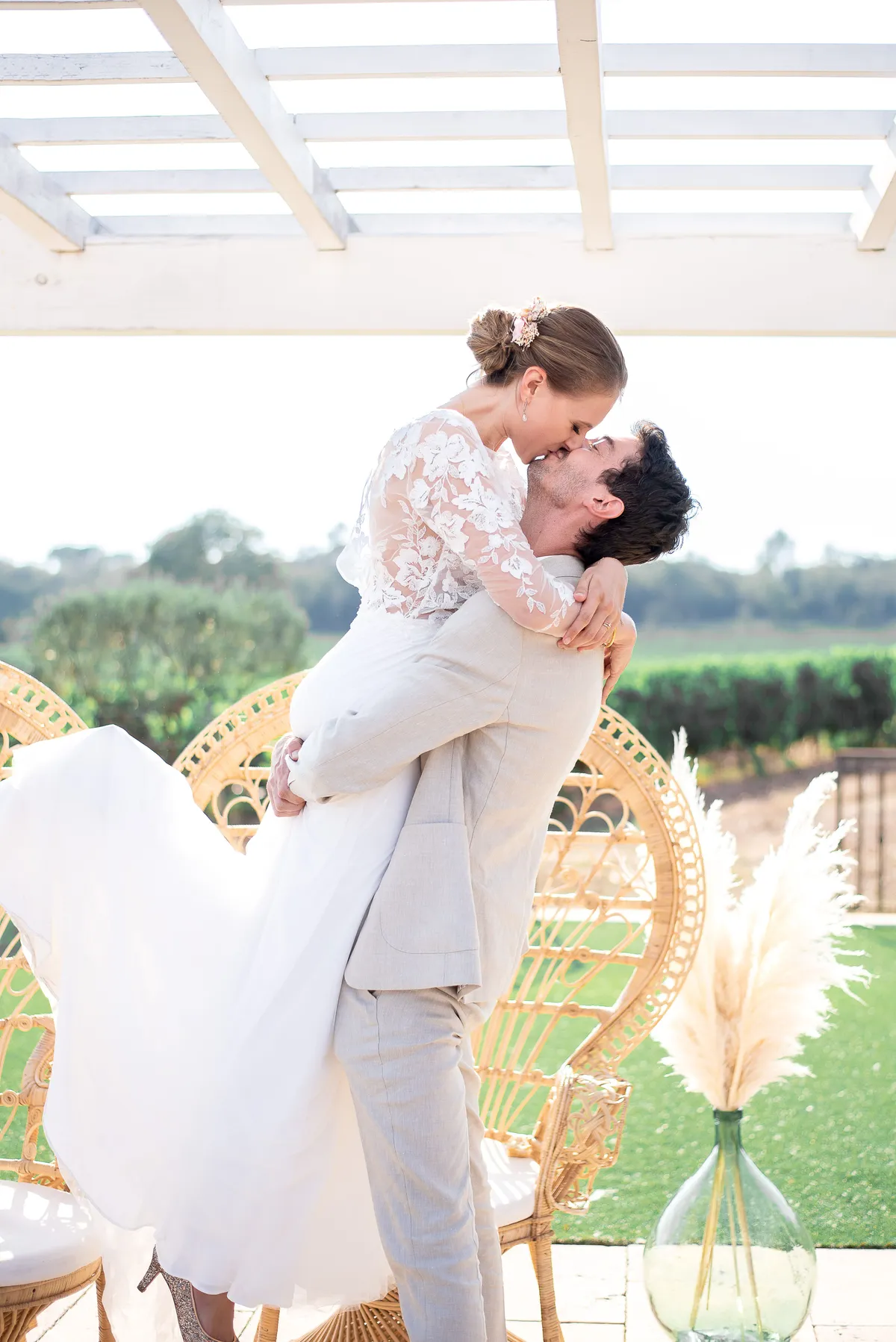 Mariage champêtre : Le mari soulève sa mariée dans un moment tendre et romantique devant un paysage verdoyant.