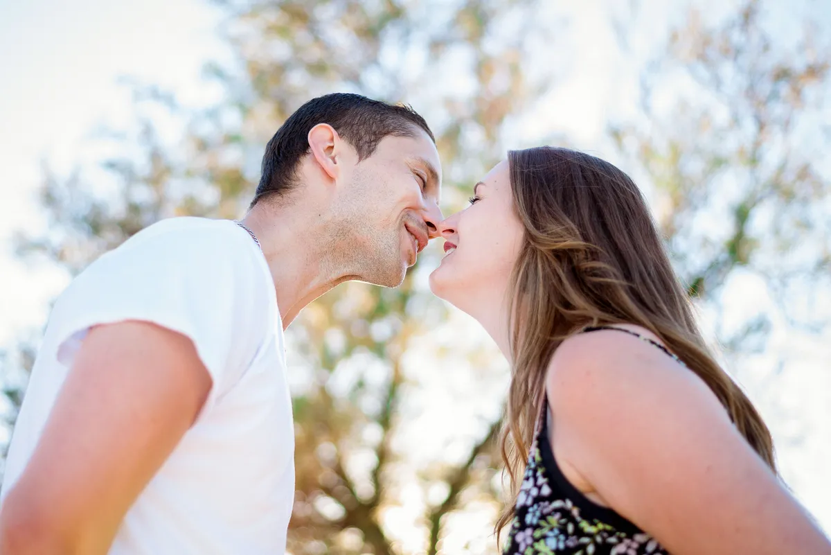 Couple s'embrassant dans un environnement ensoleillé et arboré.