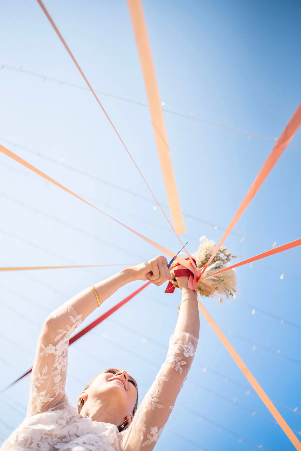 Mariée tenant son bouquet, avec des rubans orange dans le ciel bleu.
