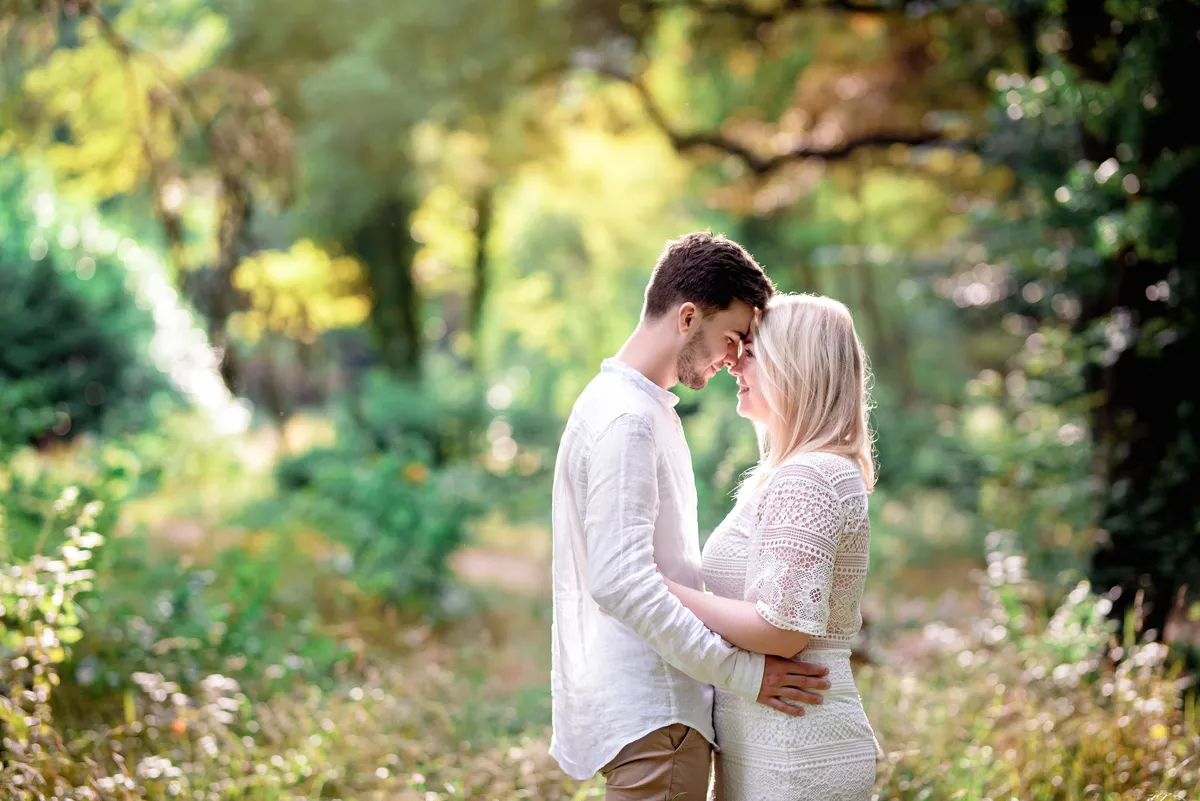 Un couple se tient ensemble dans un sous-bois fleuri, baigné de lumière naturelle.