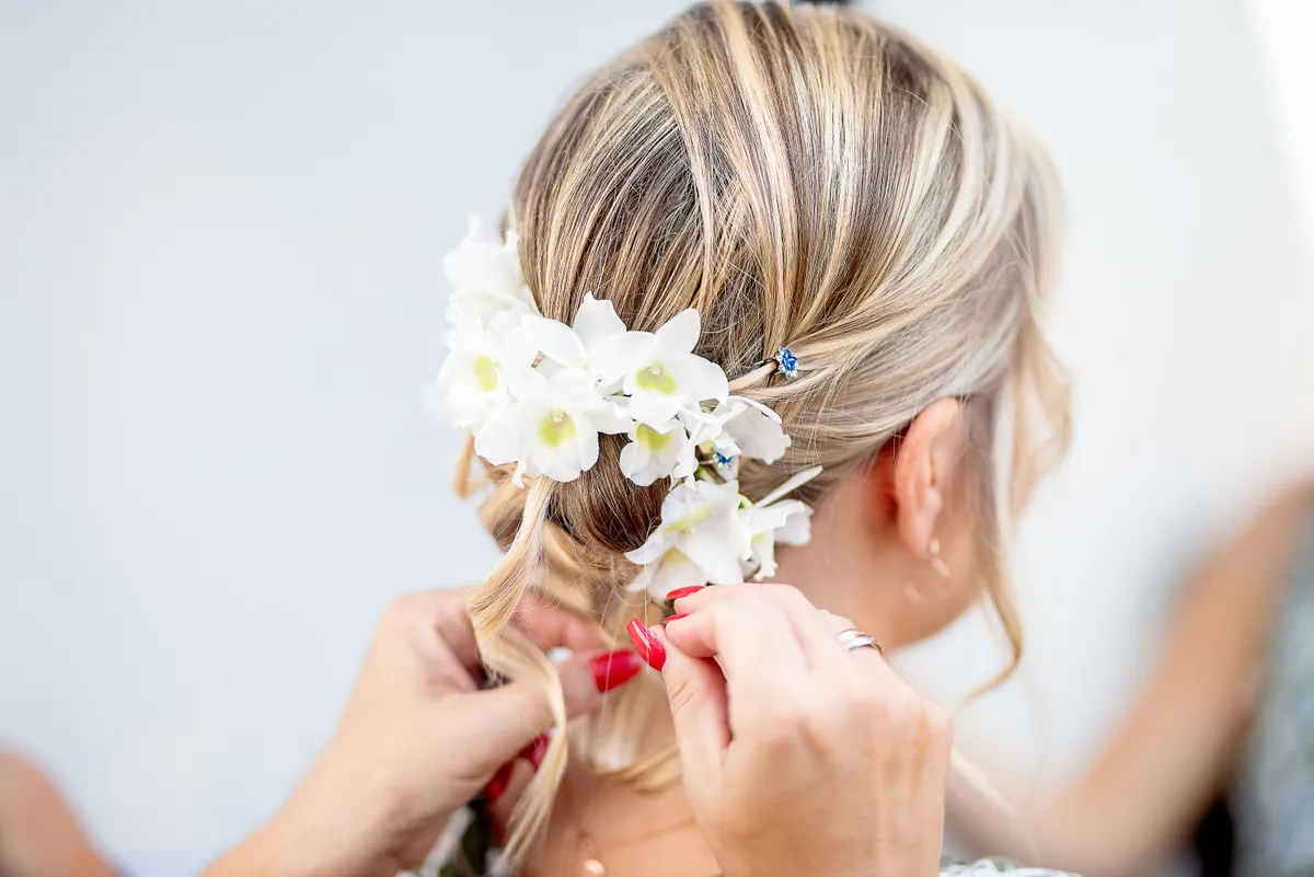 Une coiffure délicate avec des fleurs blanches, préparant l'arrivée de la mariée.