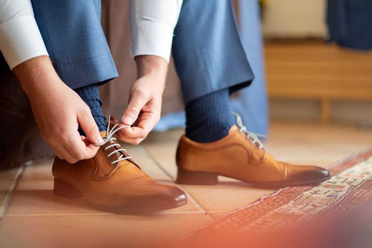 Un marié ajuste ses chaussures en cuir marron, préparant l'événement.