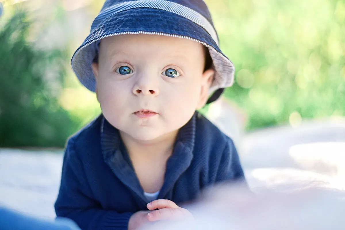 Bébé au sol, regardant vers le haut, vêtement bleu foncé et couvre-chef rayé.