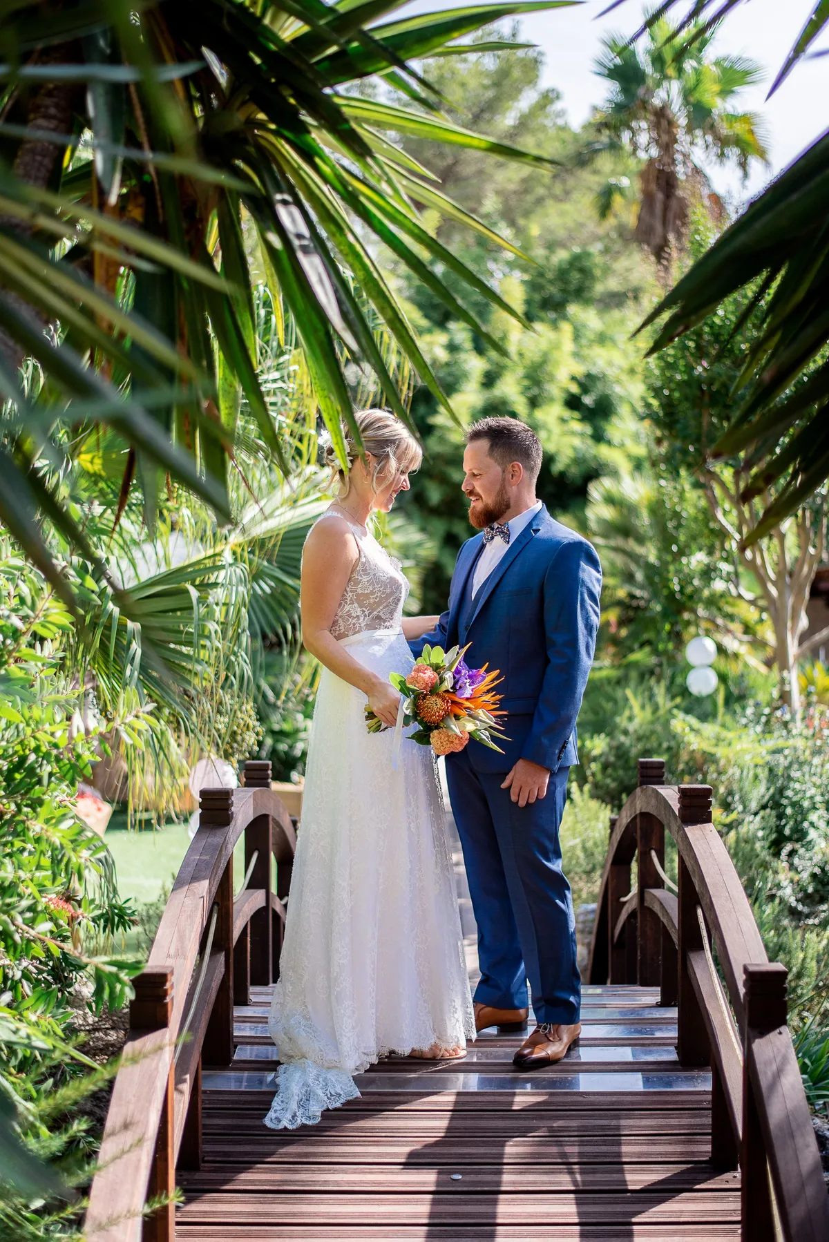 Mariés sous un pont en bois dans un jardin luxuriant.