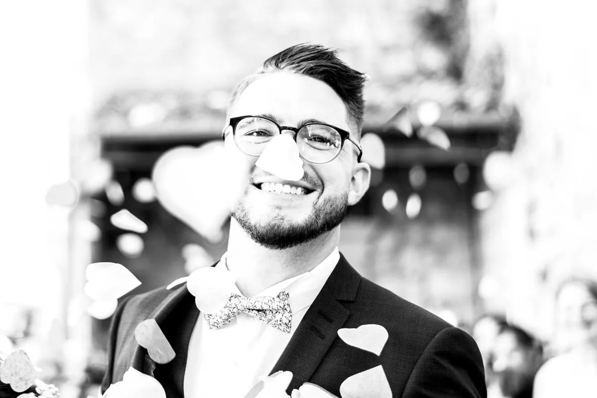 Marié souriant au milieu de pétales de roses, dans un cadre boisé et romantique.