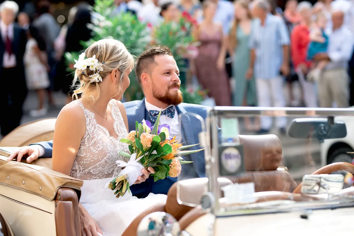 Mariés dans une ancienne voiture classique, le couple profite d'un moment romantique sous le soleil.