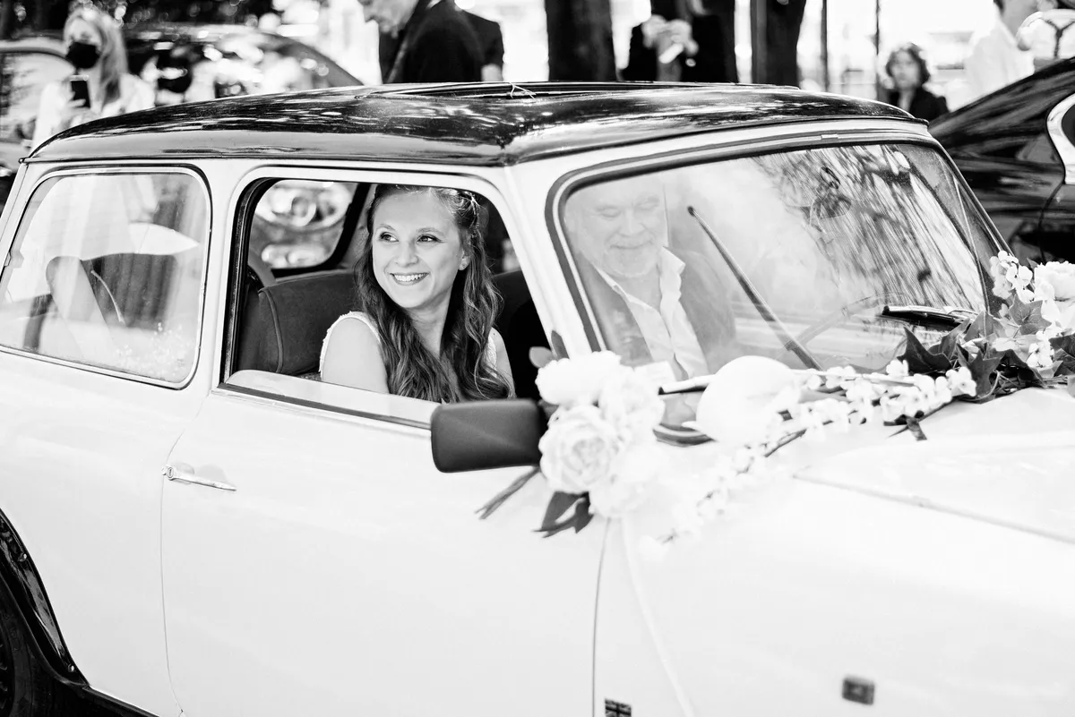 Mariée dans une vieille voiture blanche ornée de fleurs blanches.