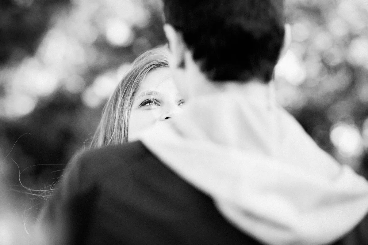 Couple au premier plan, l'épouse est tournée vers le spectateur, son visage partiellement caché par l'épaule de son mari. Le tout est drapé dans un fond boisé flou.