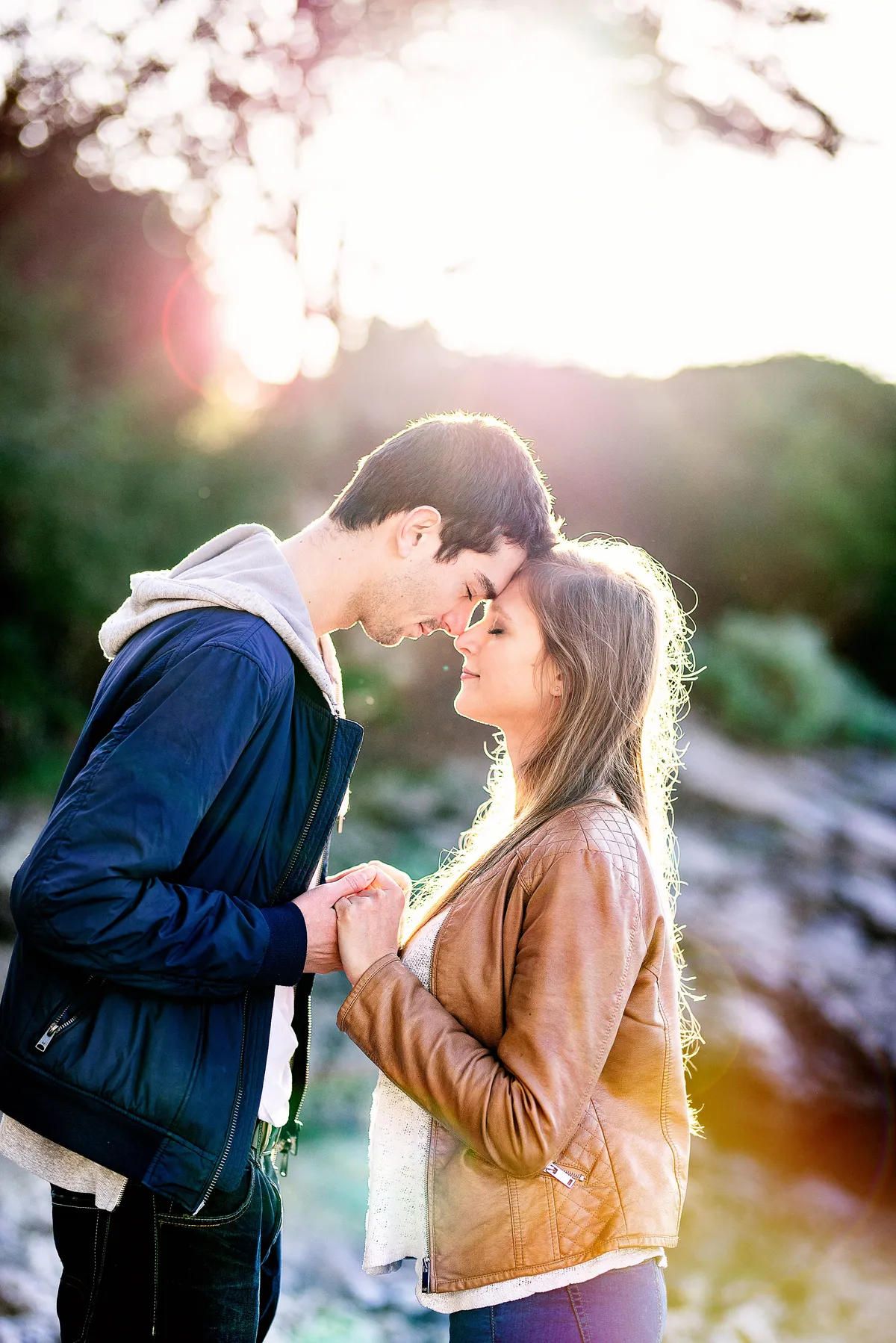 Couple amoureux se tenant la main dans un paysage montagneux baigné de lumière dorée. Ils se sont rapprochés et se sont embrassés.