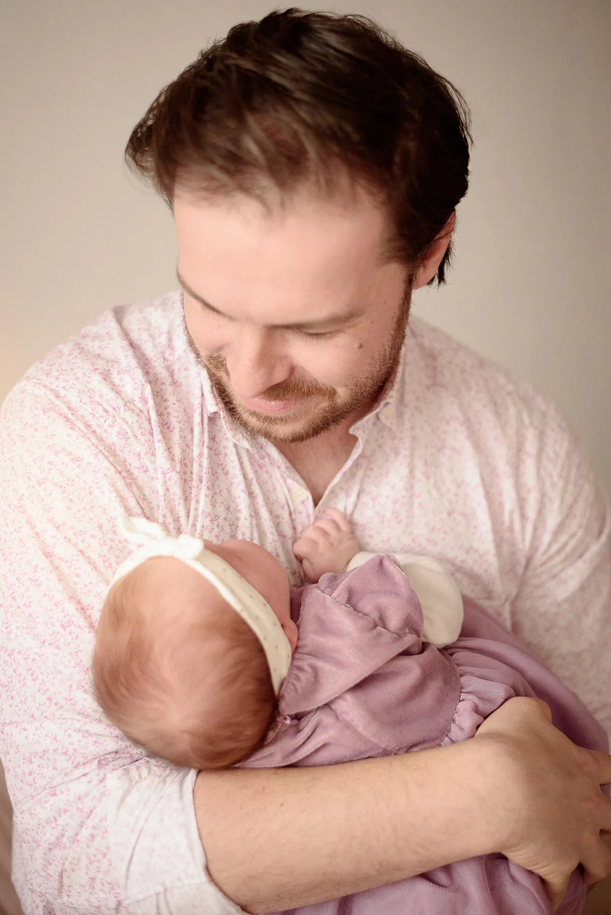 Un père serre tendrement son nouveau-né dans ses bras, vêtu d'une chemise à motifs délicats.
