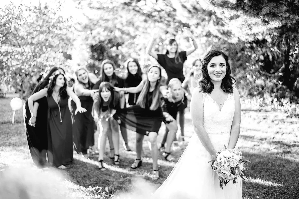Mariée au milieu de ses demoiselles d'honneur, tenant un bouquet de fleurs blanches.