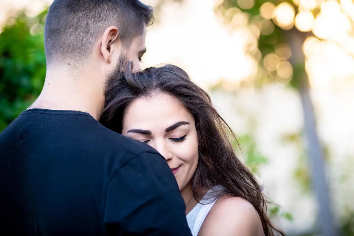 Couple enlacé dans un environnement boisé ensoleillé.