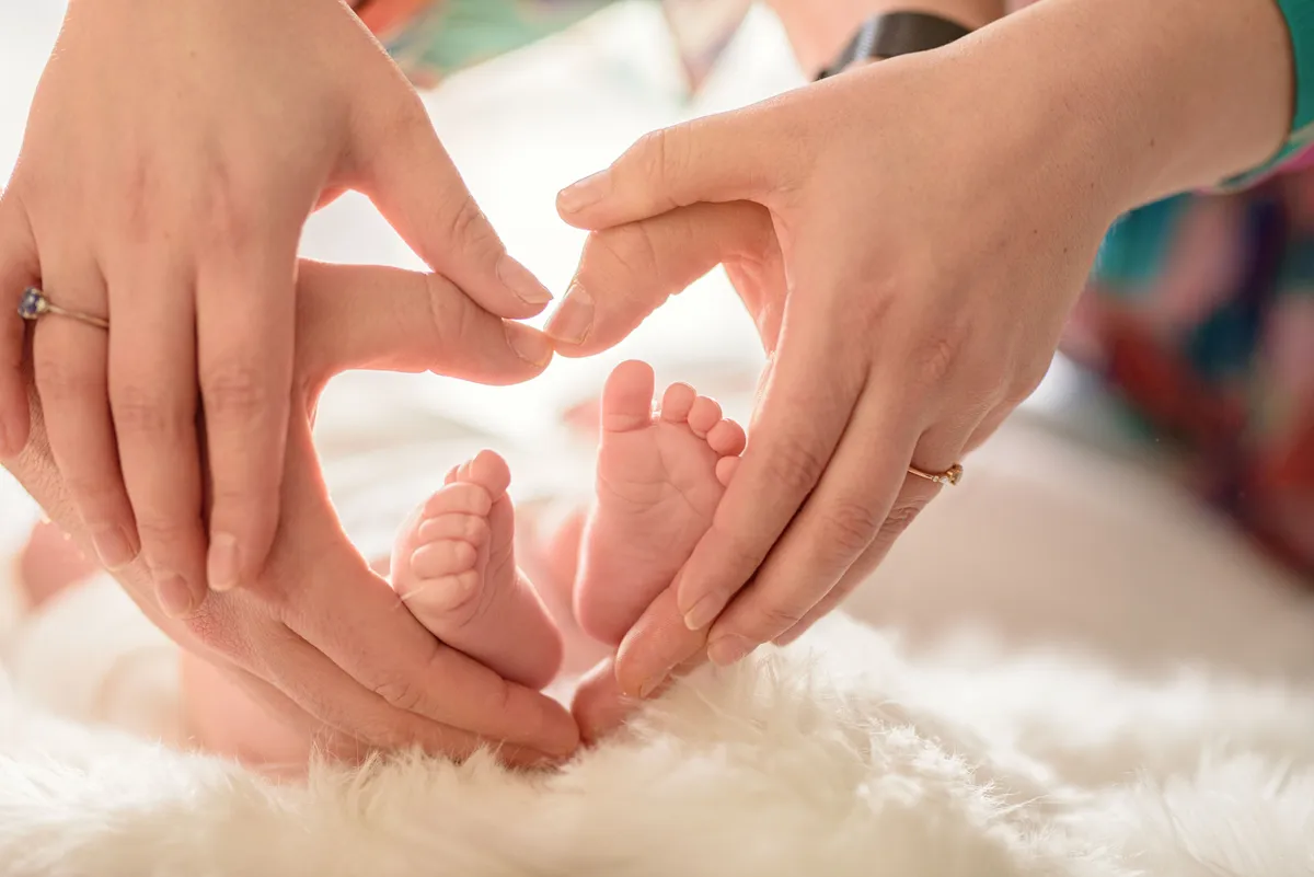 Une main tenant délicatement les petits pieds d'un bébé, formant un cœur.