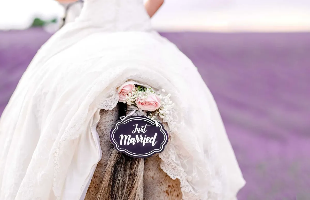 Mariée dans une longue robe blanche à crinoline, ornée d'un petit panneau en bois décoré de dentelle et d'un assortiment de roses blanches et roses.